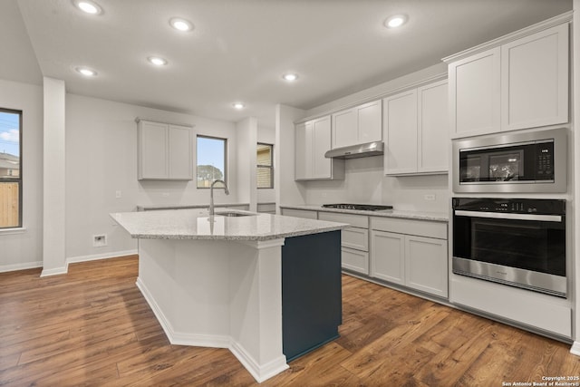 kitchen featuring built in microwave, sink, white cabinetry, stainless steel oven, and a center island with sink