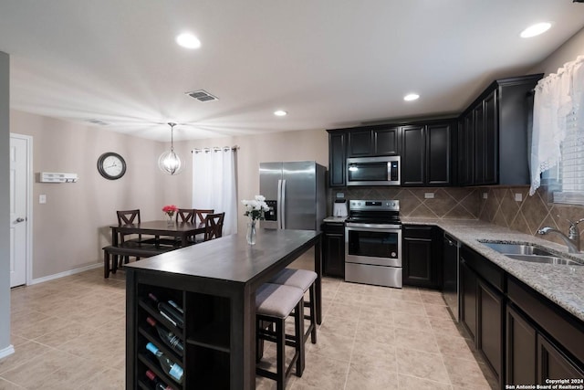 kitchen with pendant lighting, backsplash, sink, light stone counters, and stainless steel appliances