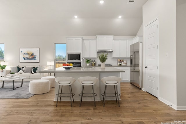 kitchen with stainless steel refrigerator with ice dispenser, built in microwave, a kitchen island with sink, and white cabinets