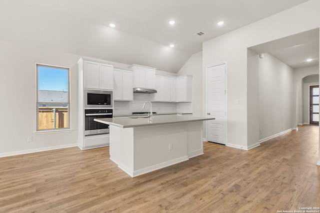 kitchen featuring built in microwave, sink, white cabinetry, stainless steel oven, and an island with sink