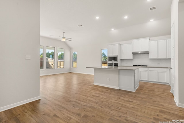 kitchen featuring sink, vaulted ceiling, white cabinets, and a center island with sink