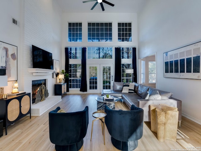 living room with ceiling fan, a towering ceiling, light hardwood / wood-style flooring, and a brick fireplace