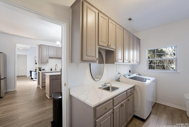 clothes washing area featuring cabinets, separate washer and dryer, light hardwood / wood-style floors, and sink