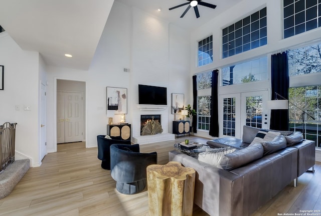 living room with a fireplace, a high ceiling, light hardwood / wood-style floors, and ceiling fan