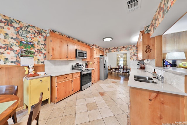 kitchen featuring light tile patterned floors, stainless steel appliances, wood walls, and sink