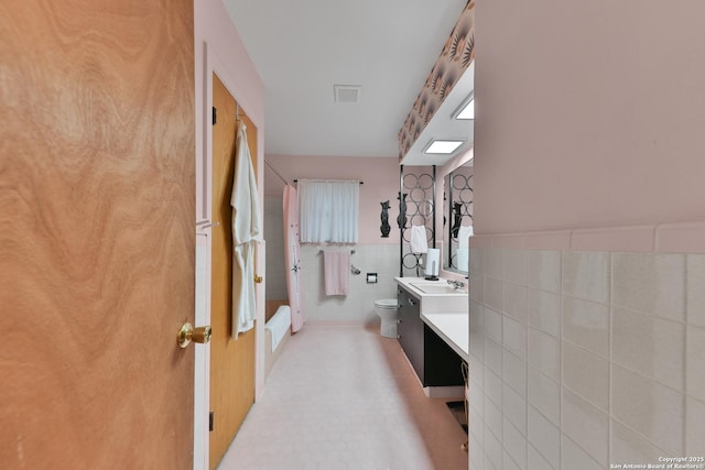 bathroom featuring vanity, toilet, and tile walls