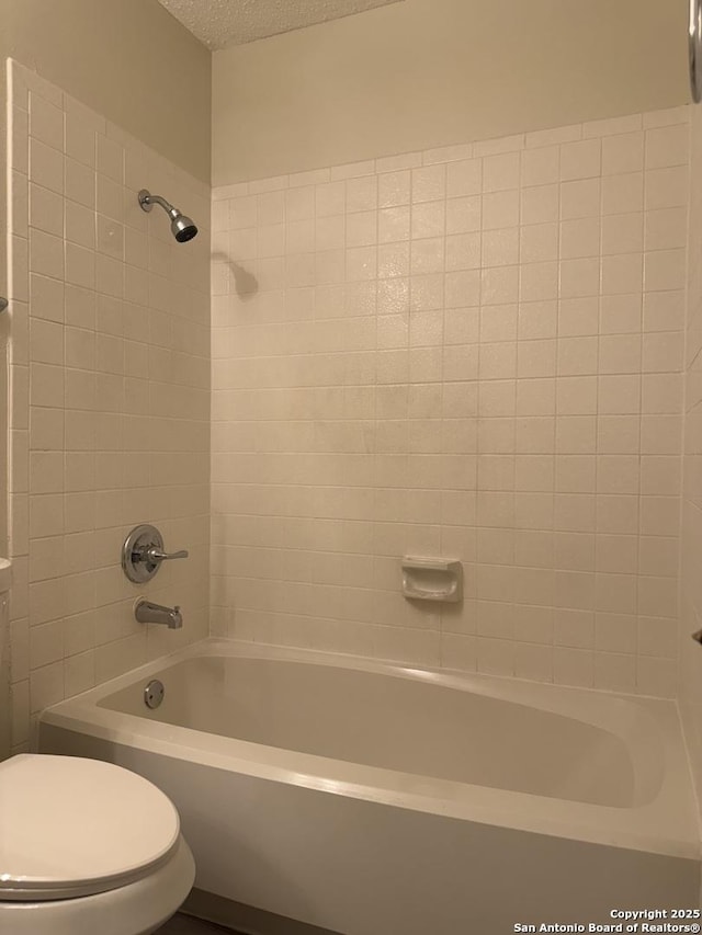 bathroom with a textured ceiling, toilet, and tiled shower / bath