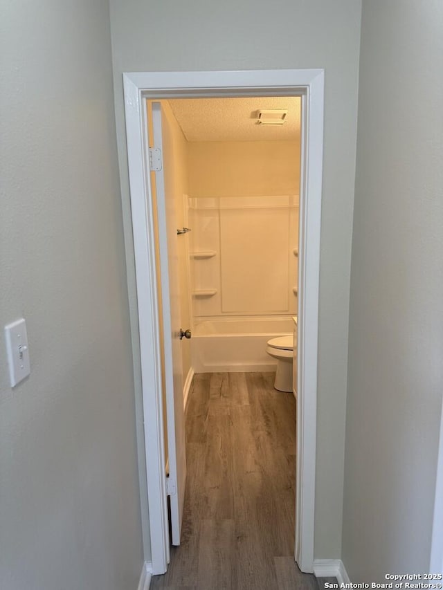 bathroom with hardwood / wood-style floors, washtub / shower combination, and toilet