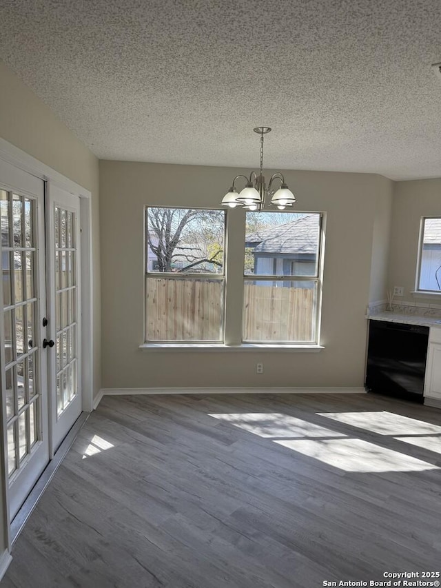 unfurnished dining area with hardwood / wood-style flooring, french doors, a textured ceiling, and a notable chandelier