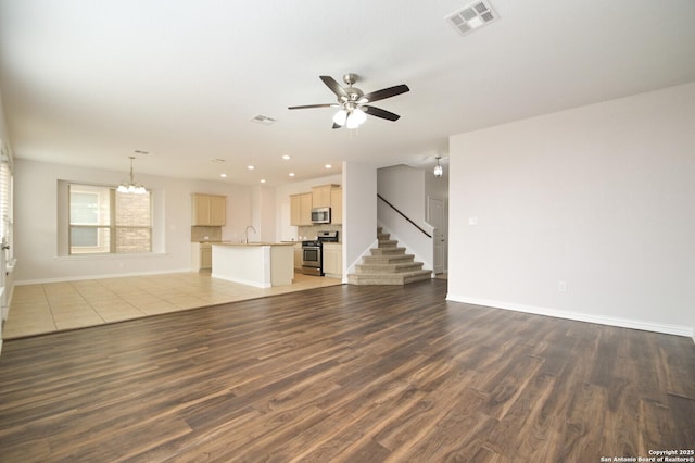 unfurnished living room featuring sink, dark wood-type flooring, and ceiling fan with notable chandelier