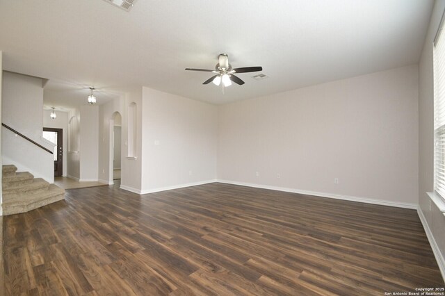 empty room featuring a wealth of natural light, ceiling fan, and dark wood-type flooring