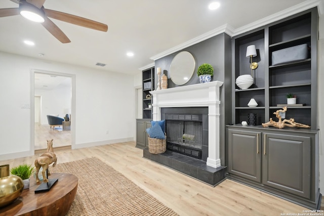 living room featuring light hardwood / wood-style floors, built in features, ceiling fan, and a tiled fireplace