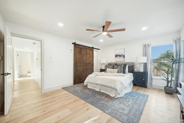 bedroom with a barn door, ceiling fan, and light hardwood / wood-style flooring