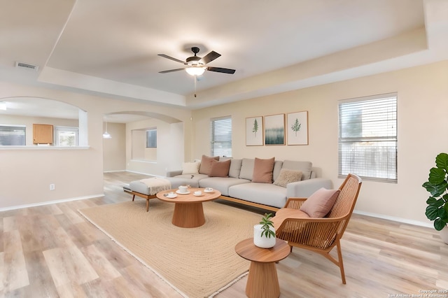 living room with a tray ceiling, a healthy amount of sunlight, and light hardwood / wood-style floors