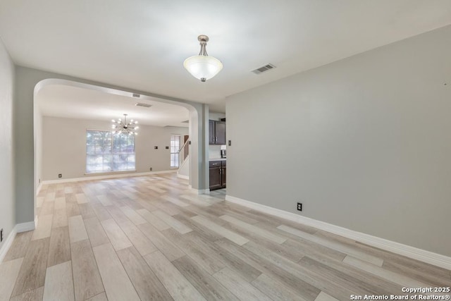 spare room with a notable chandelier and light wood-type flooring