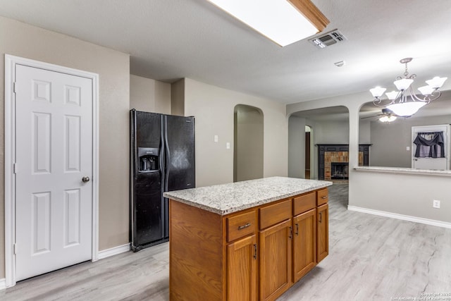 kitchen with hanging light fixtures, black fridge, a notable chandelier, a fireplace, and a kitchen island