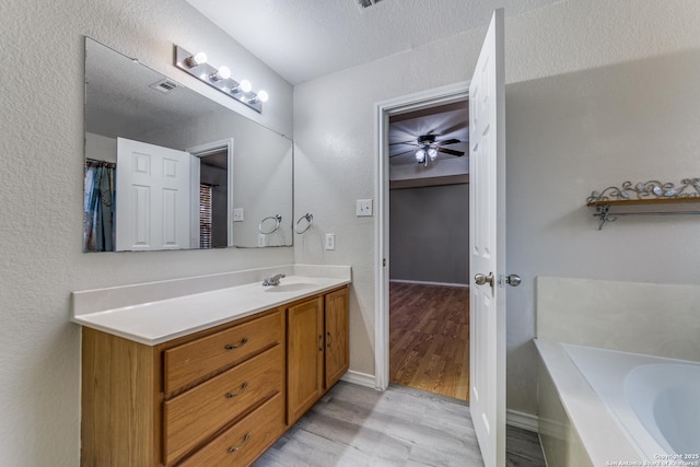 bathroom with a washtub, vanity, a textured ceiling, ceiling fan, and wood-type flooring