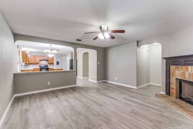 unfurnished living room with a fireplace, ceiling fan with notable chandelier, light hardwood / wood-style flooring, and sink