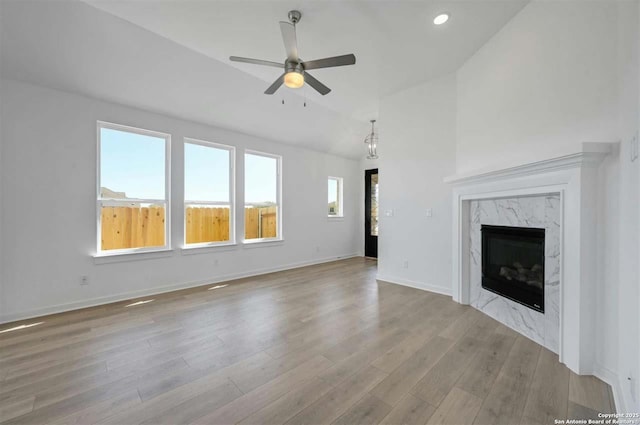 unfurnished living room featuring ceiling fan, light wood-type flooring, a high end fireplace, and vaulted ceiling