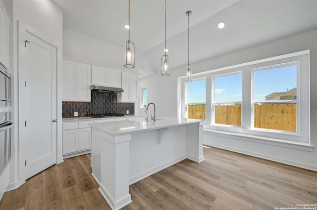 kitchen featuring black gas stovetop, decorative light fixtures, white cabinets, lofted ceiling, and an island with sink