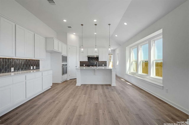 kitchen with stainless steel appliances, vaulted ceiling, white cabinetry, hanging light fixtures, and an island with sink