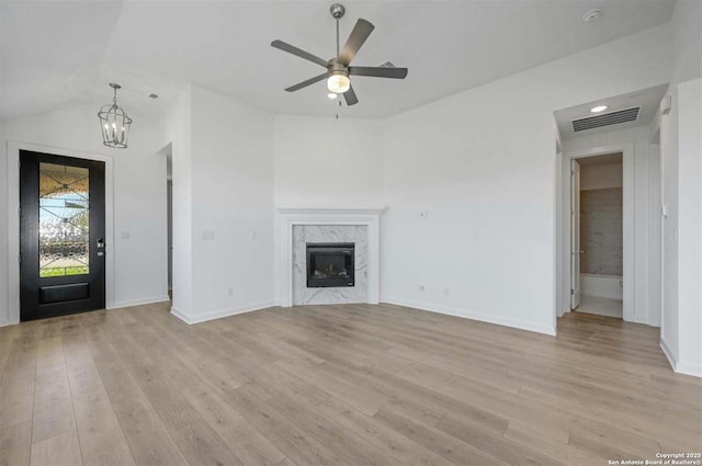 unfurnished living room featuring ceiling fan with notable chandelier, light wood-type flooring, a fireplace, and vaulted ceiling