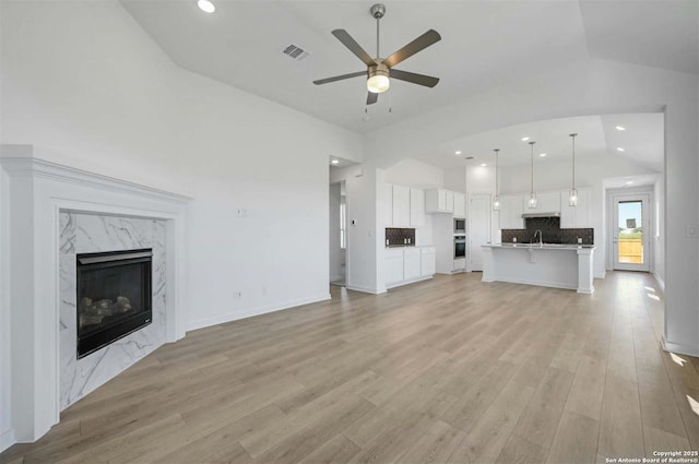 unfurnished living room with ceiling fan, sink, light hardwood / wood-style flooring, a premium fireplace, and lofted ceiling