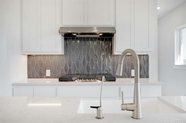 kitchen featuring ventilation hood, decorative backsplash, light stone counters, and white cabinetry