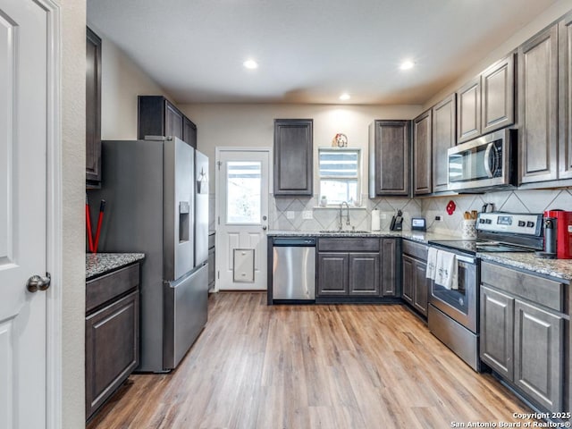 kitchen with sink, tasteful backsplash, light stone counters, light hardwood / wood-style floors, and appliances with stainless steel finishes