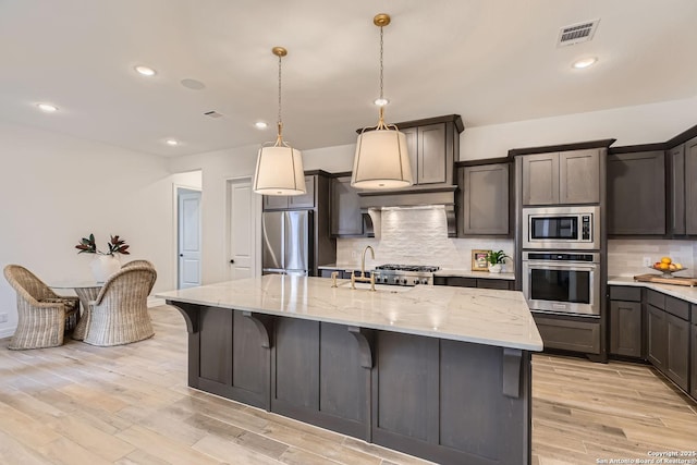 kitchen featuring decorative light fixtures, appliances with stainless steel finishes, tasteful backsplash, and a kitchen island with sink