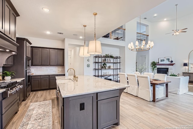 kitchen featuring light stone countertops, sink, stainless steel appliances, hanging light fixtures, and ceiling fan with notable chandelier