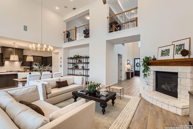 living room featuring a stone fireplace, a towering ceiling, light wood-type flooring, and an inviting chandelier