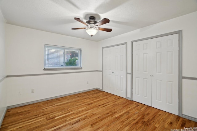 unfurnished bedroom with hardwood / wood-style flooring, ceiling fan, and two closets