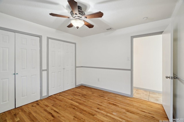 unfurnished bedroom featuring ceiling fan, wood-type flooring, and multiple closets