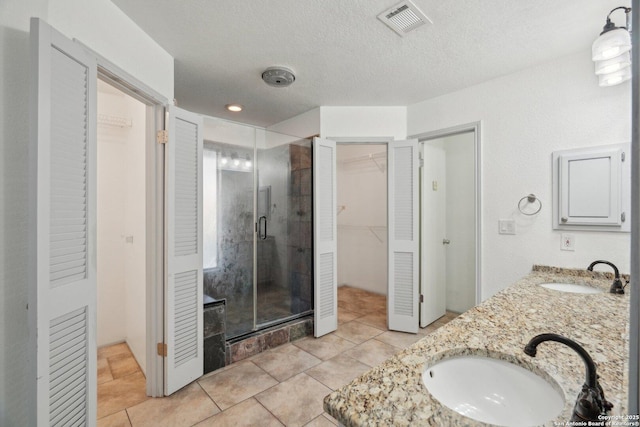 bathroom featuring vanity, a textured ceiling, tile patterned floors, and a shower with door