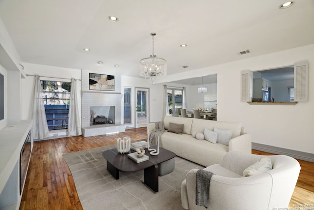 living room with an inviting chandelier, light wood-type flooring, and a brick fireplace