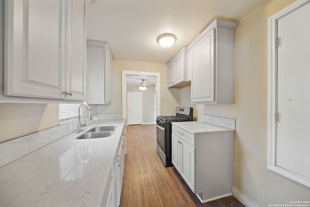 kitchen featuring light stone countertops, stainless steel gas range oven, sink, hardwood / wood-style floors, and white cabinetry