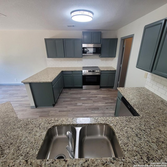 kitchen with kitchen peninsula, light stone countertops, stainless steel appliances, and decorative backsplash