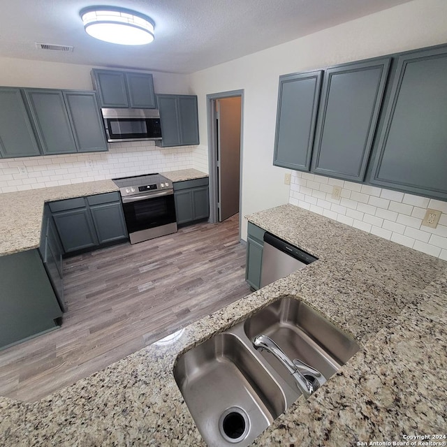 kitchen featuring appliances with stainless steel finishes, tasteful backsplash, light stone counters, and sink