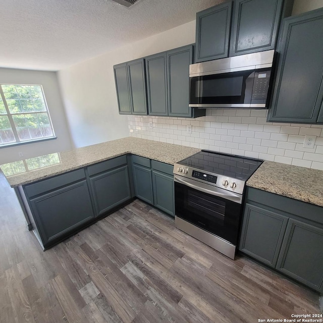 kitchen featuring kitchen peninsula, appliances with stainless steel finishes, backsplash, and dark hardwood / wood-style flooring