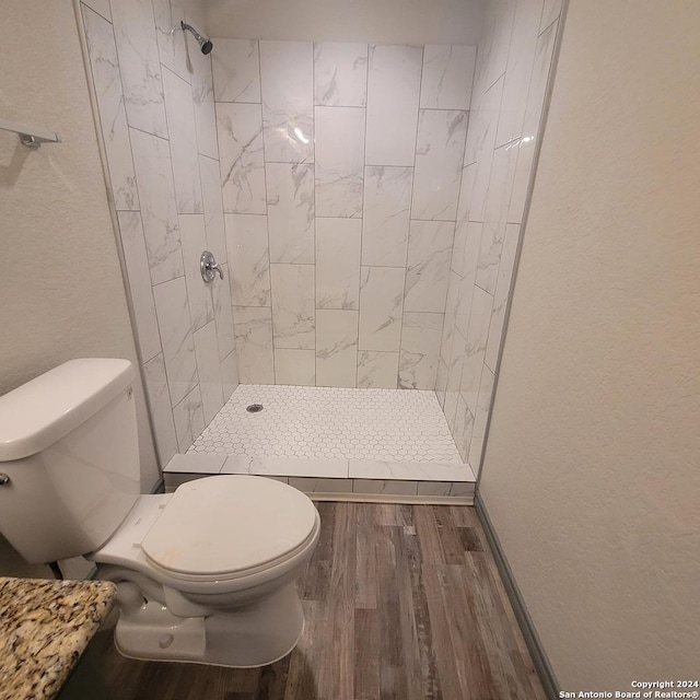 bathroom featuring a tile shower, hardwood / wood-style floors, and toilet