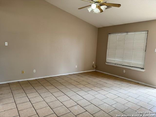 empty room with lofted ceiling, ceiling fan, and baseboards