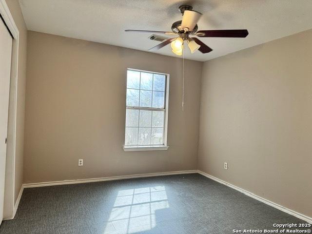 spare room with dark colored carpet, a ceiling fan, visible vents, and baseboards