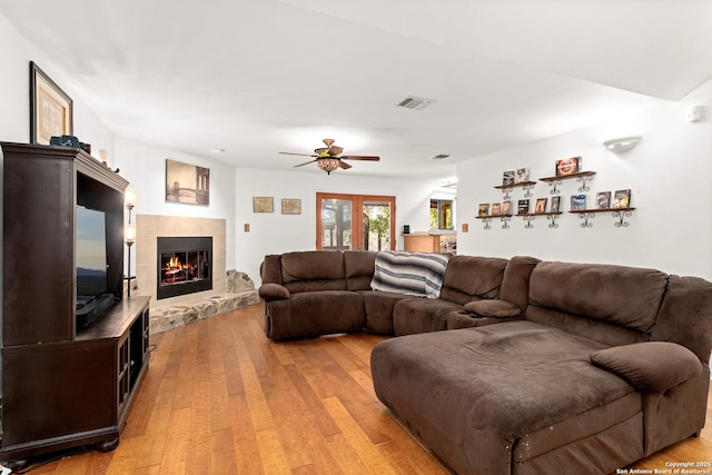 living room with a tile fireplace, french doors, light wood-type flooring, and ceiling fan