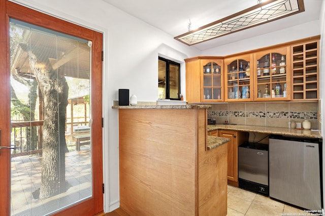 bar with decorative backsplash, light stone counters, light tile patterned floors, and fridge