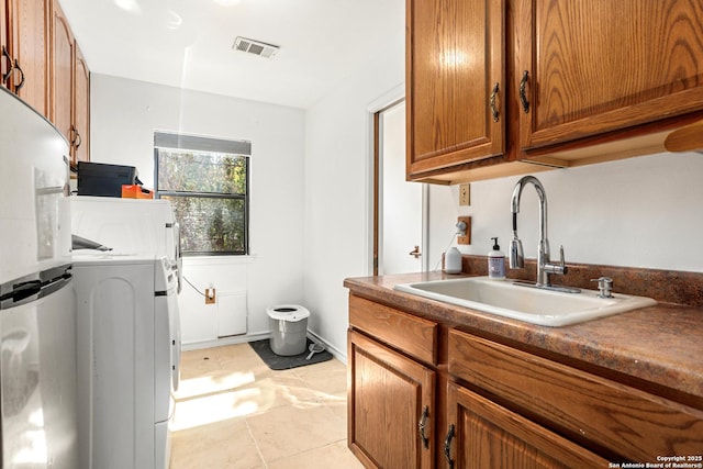 kitchen featuring stainless steel fridge, sink, light tile patterned floors, and washer / dryer