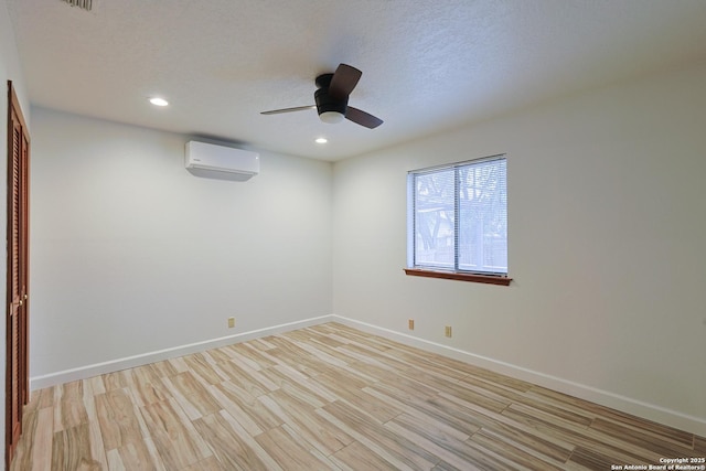 unfurnished room featuring a textured ceiling, light hardwood / wood-style flooring, an AC wall unit, and ceiling fan