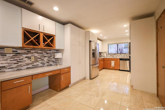 kitchen featuring decorative backsplash, appliances with stainless steel finishes, built in desk, white cabinets, and light tile patterned flooring