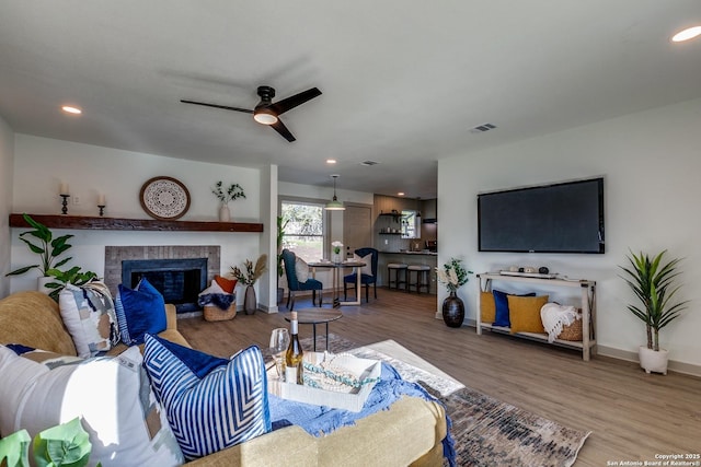 living room featuring hardwood / wood-style floors, a brick fireplace, and ceiling fan