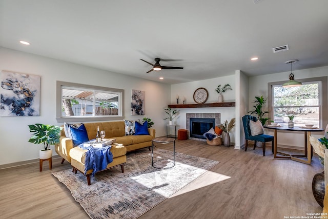 living room with ceiling fan, a tile fireplace, a wealth of natural light, and light hardwood / wood-style flooring